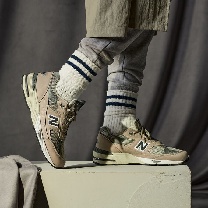 Knee-down crop of a man wearing grey NB 991 sneakers with grey joggers tucked into white crew socks with black stripes