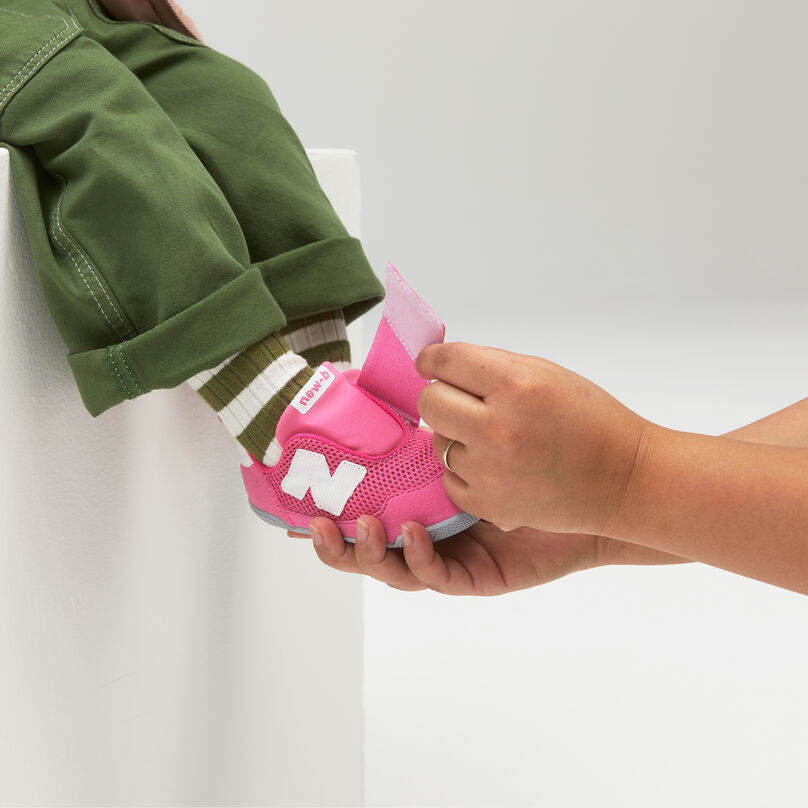 Un adulte aide un enfant à attacher ses chaussures New-B rose à fermeture Velcro