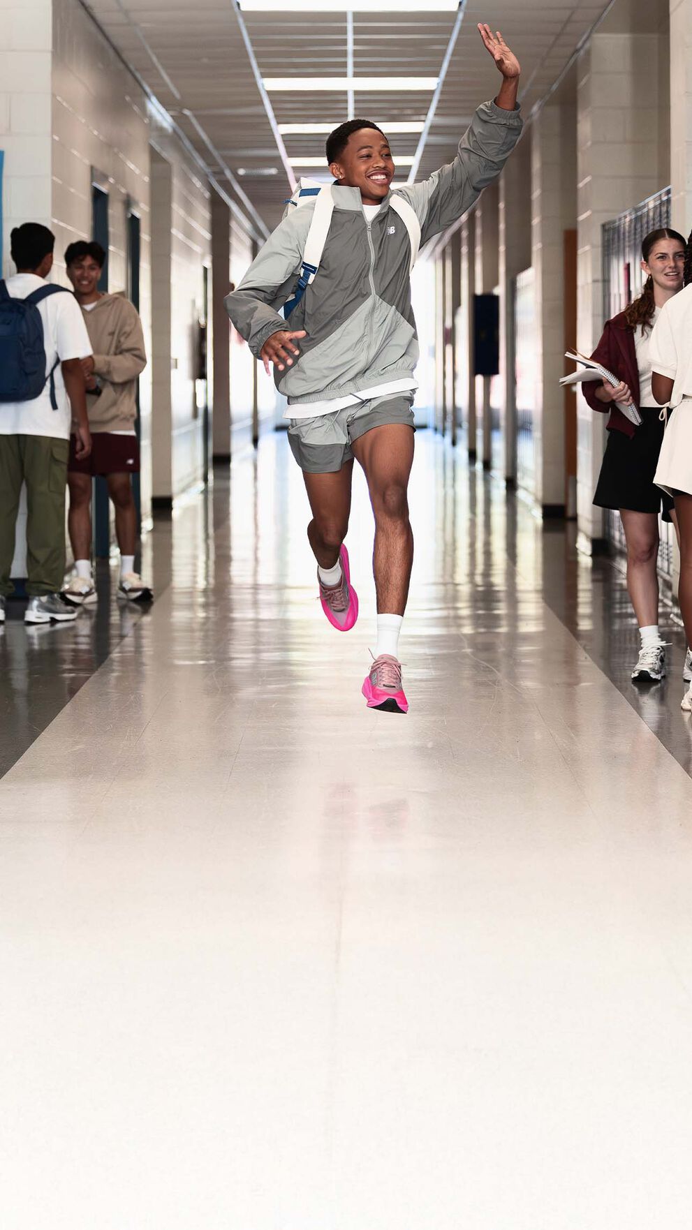 Quincy Wilson wearing the FuelCell Rebel shoes running and waving at a hallway. 