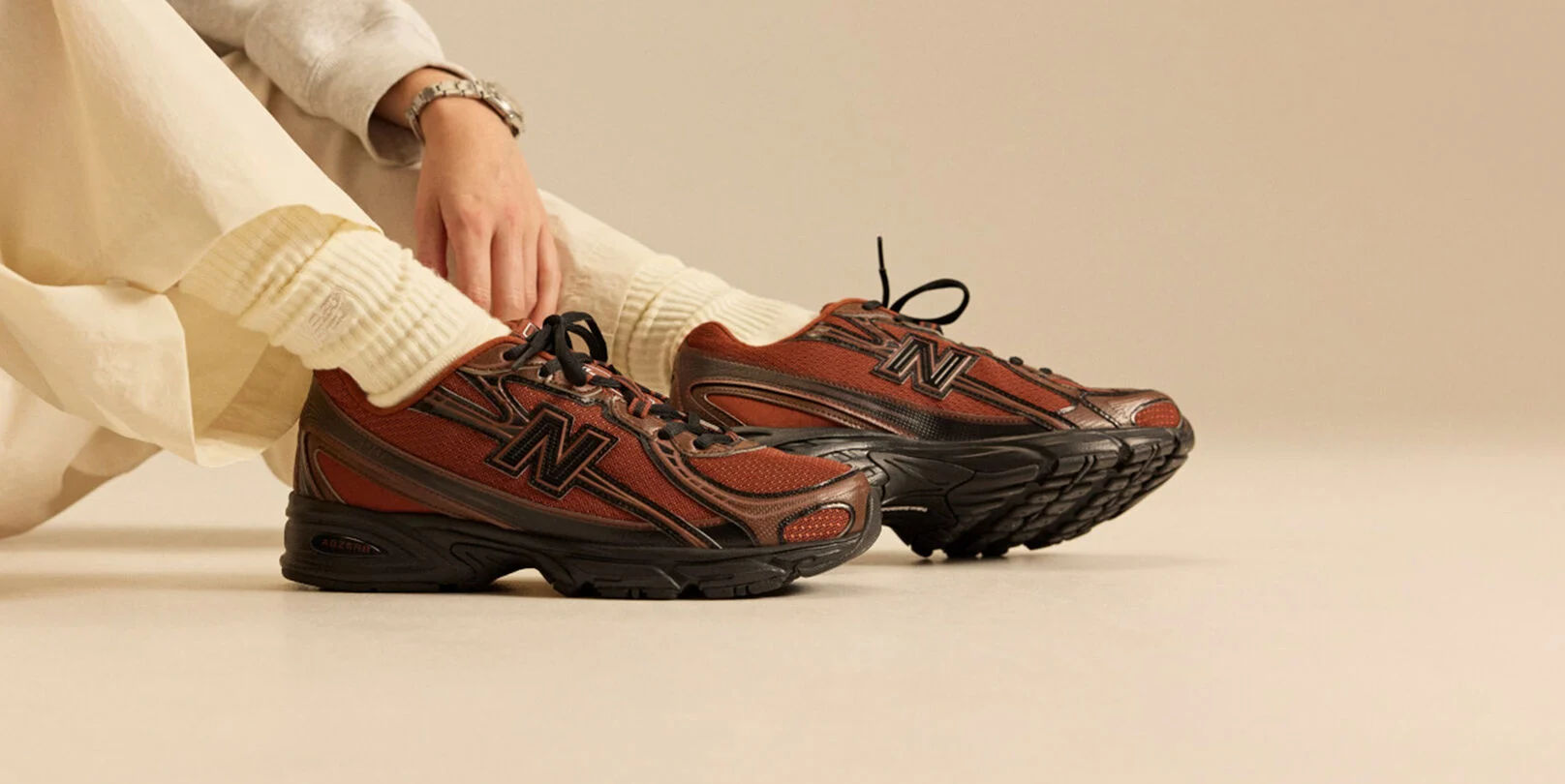 Image de quelqu&rsquo;un assis en baskets New Balance devant un fond beige.