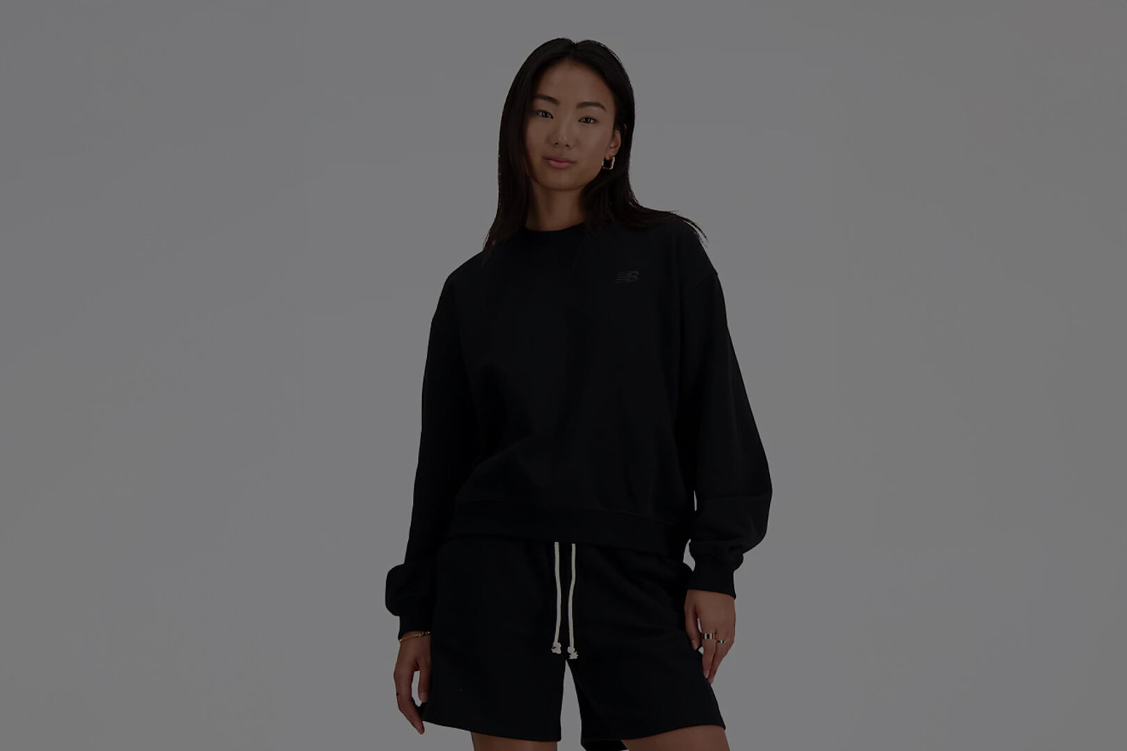Femme vêtue d'un t-shirt New Balance noir à manches longues et d'un short noir assorti.