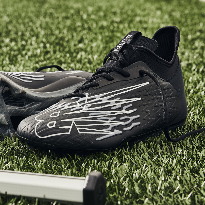 Single black cleat sitting on turf with the lateral side in focus.