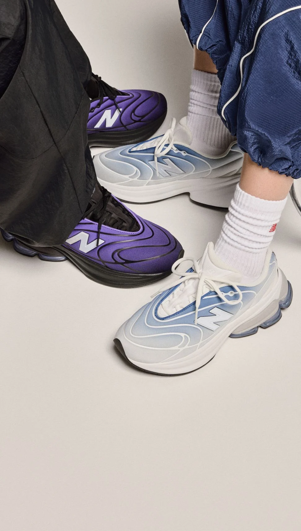 Vue des jambes (des genoux vers le bas) de deux personnes portant des espadrilles sur un fond beige. 