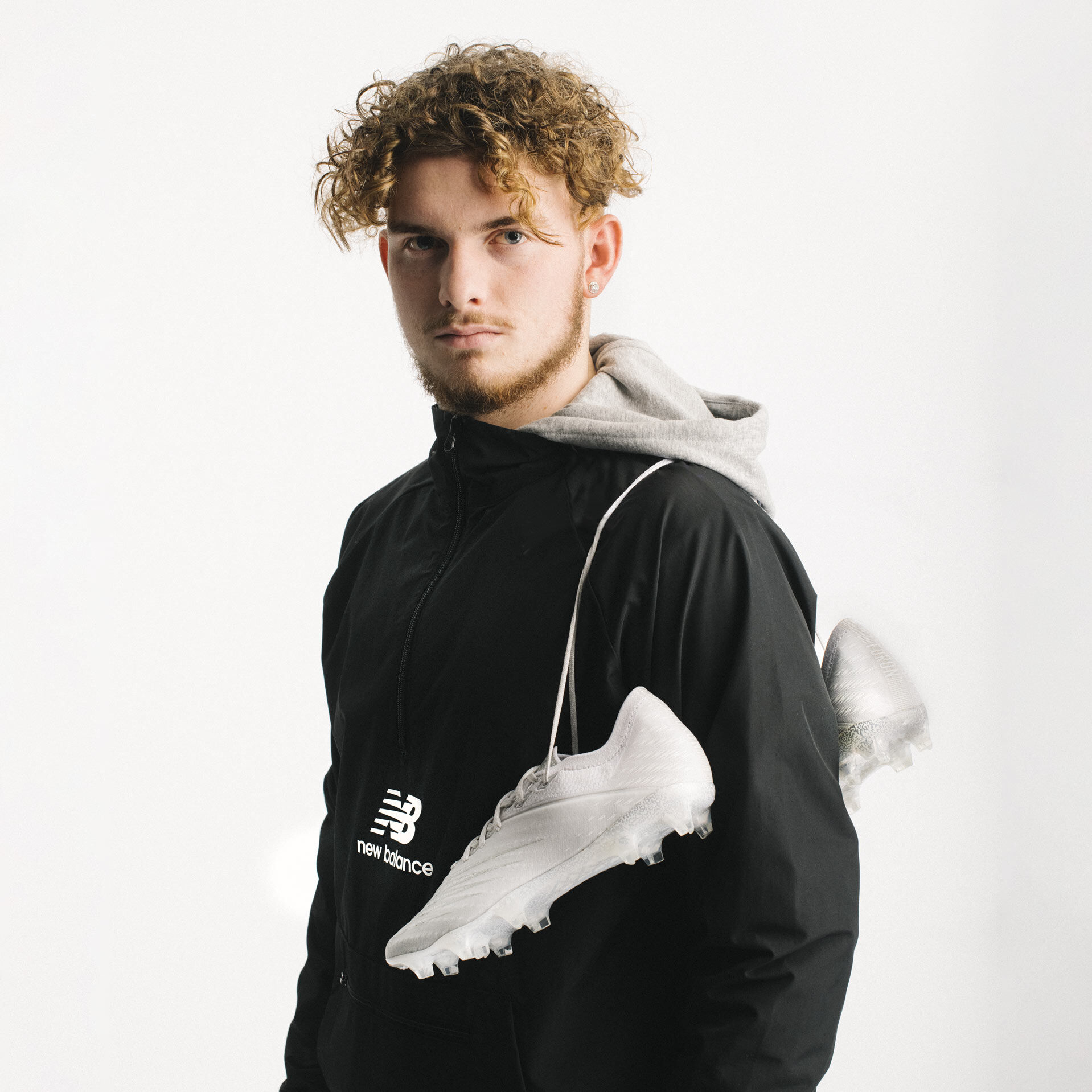 Soccer player Harvey Elliott wearing black New Balance windbreaker with pair of cleats draped over his shoulder