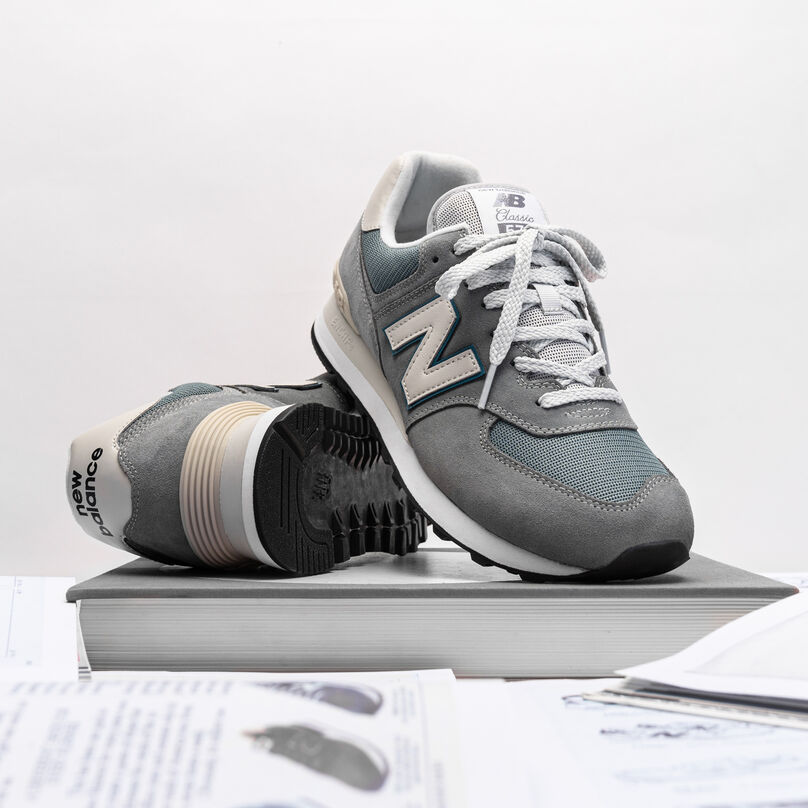 Pair of grey 574 sitting on a book with a pile of New Balance archival ads around it.