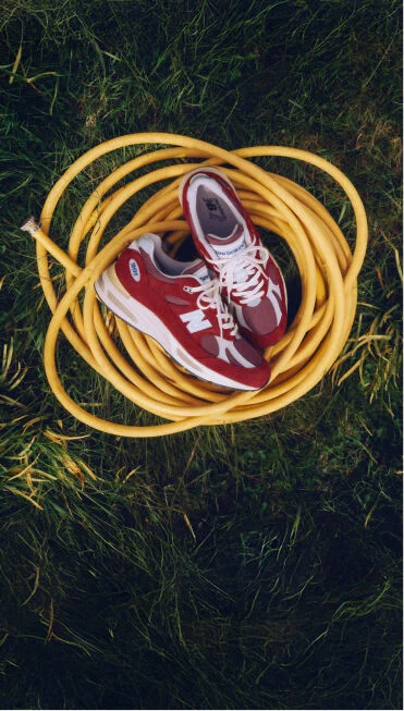 Une paire de baskets New Balance fabriqu&eacute;es au Royaume-Uni pos&eacute;e sur un tuyau enroul&eacute; jaune sur une pelouse verdoyante.