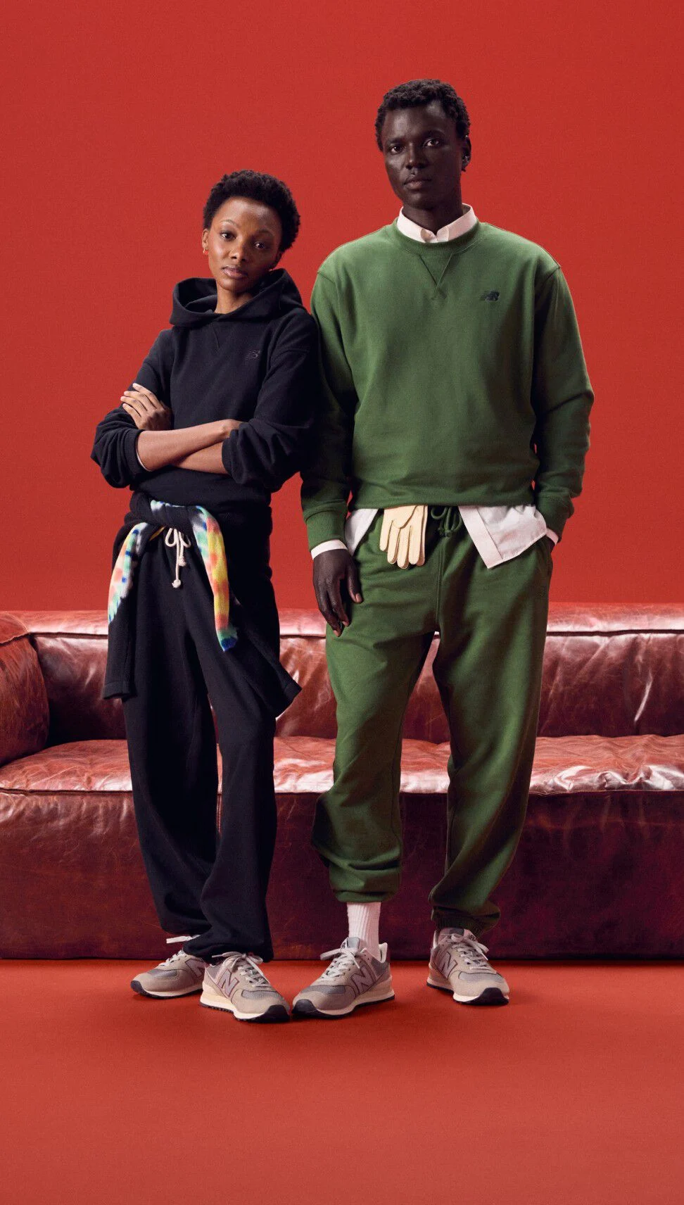 Couple wearing same color outfits standing on a red background in front of a red couch.