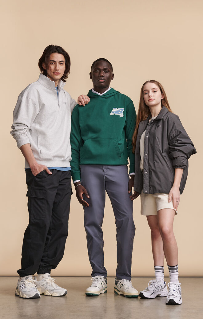 Group of men and women wearing New Balance lifestyle clothing and shoes posed against beige background in studio environment 