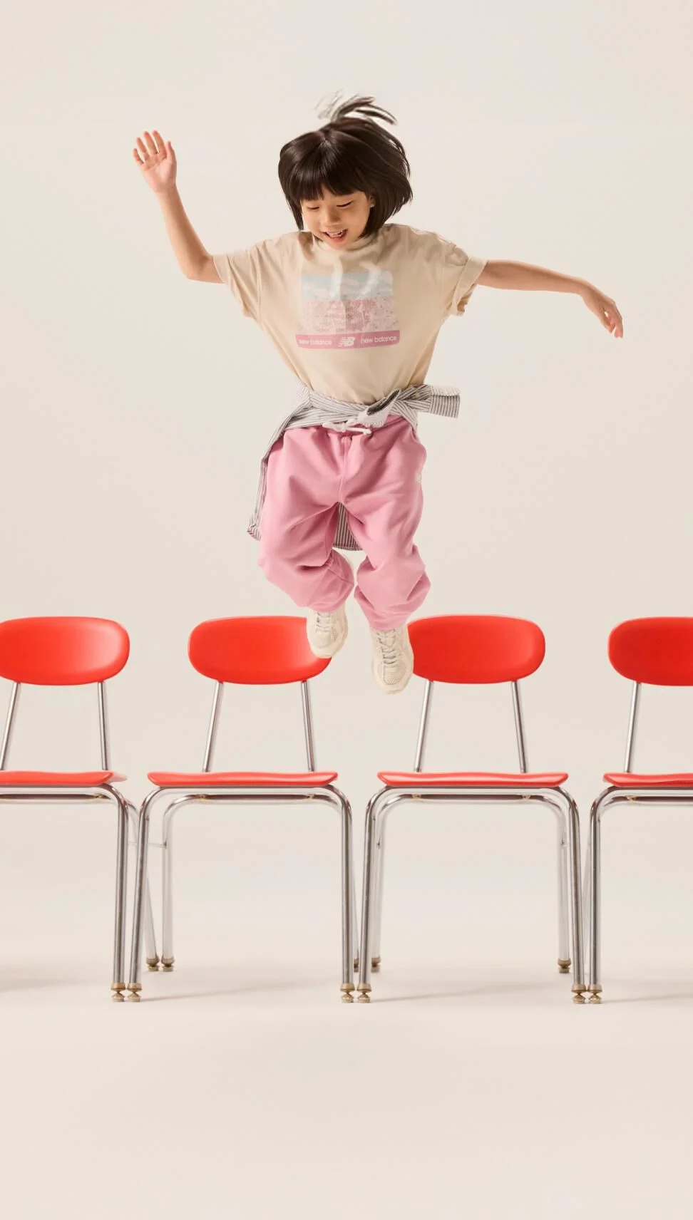 A young female in pink pants jumping off a chair. 