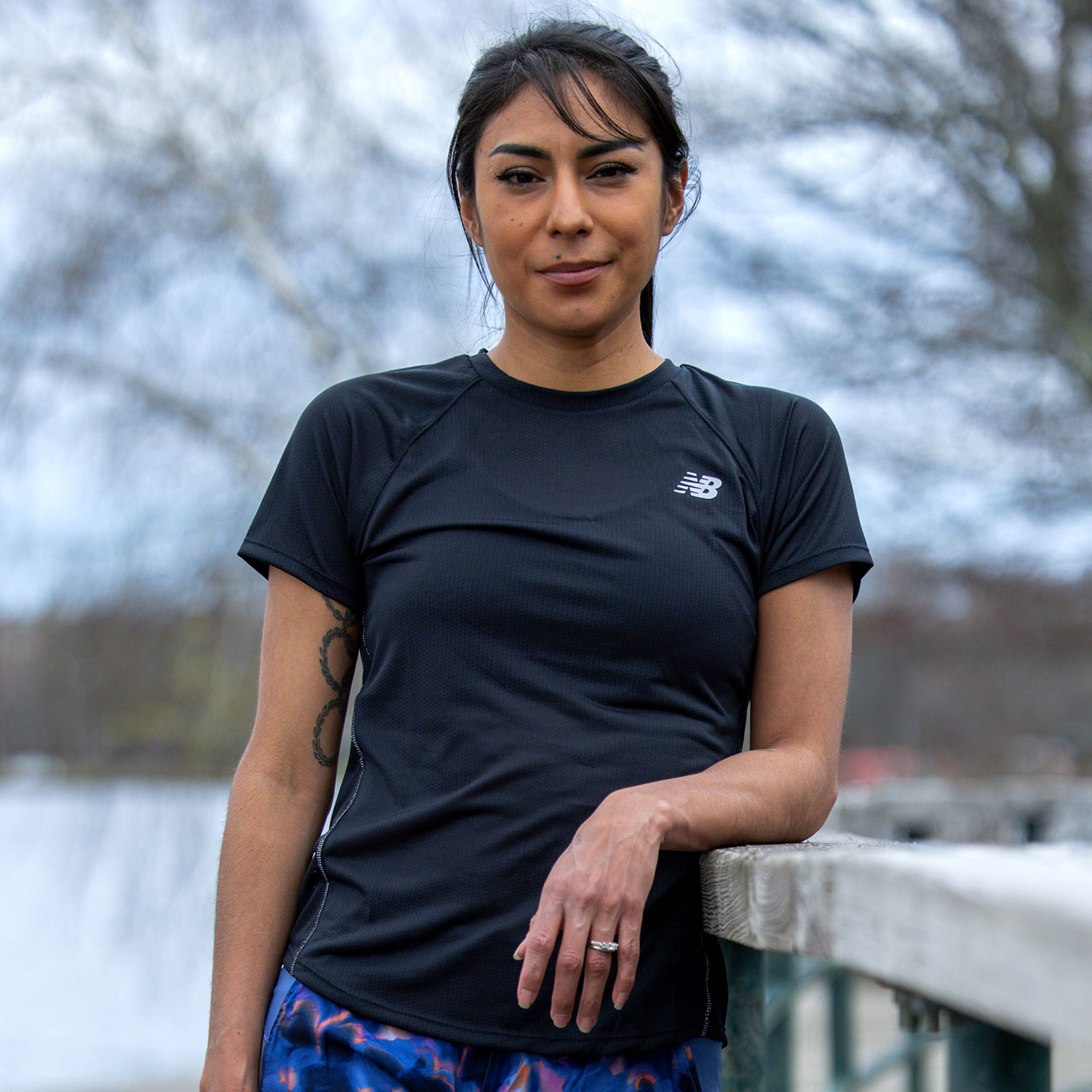 Track & Field athlete, Brenda Martinez, leaning against the wooden railing of a footbridge over a small body of water