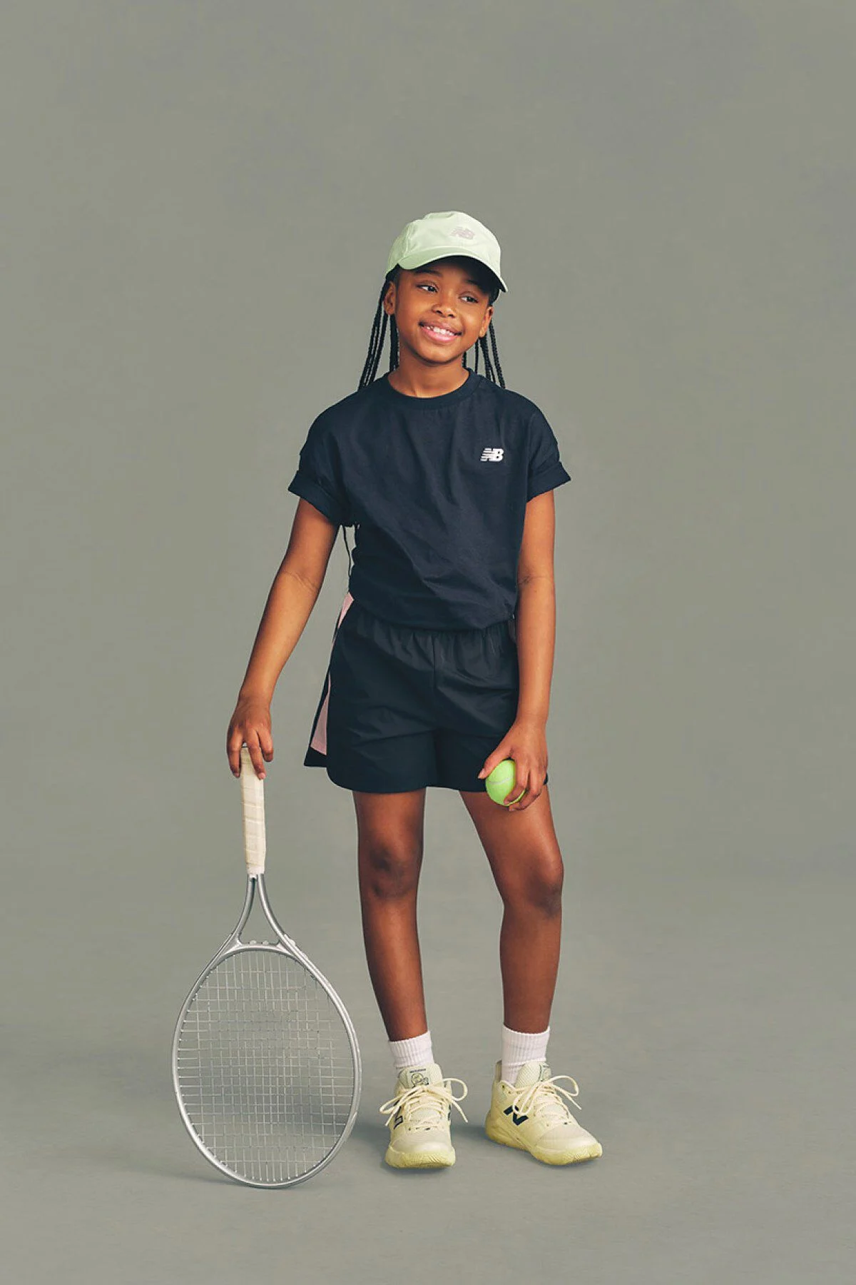 Un enfant tenant une raquette de tennis devant un fond gris de studio.
