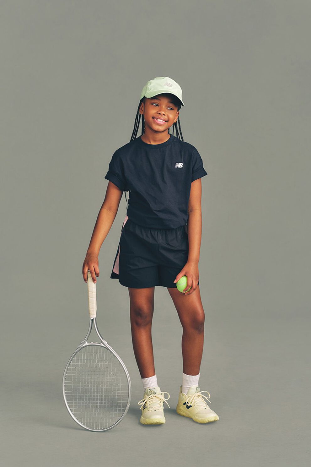 Un enfant tenant une raquette de tennis devant un fond gris de studio.
