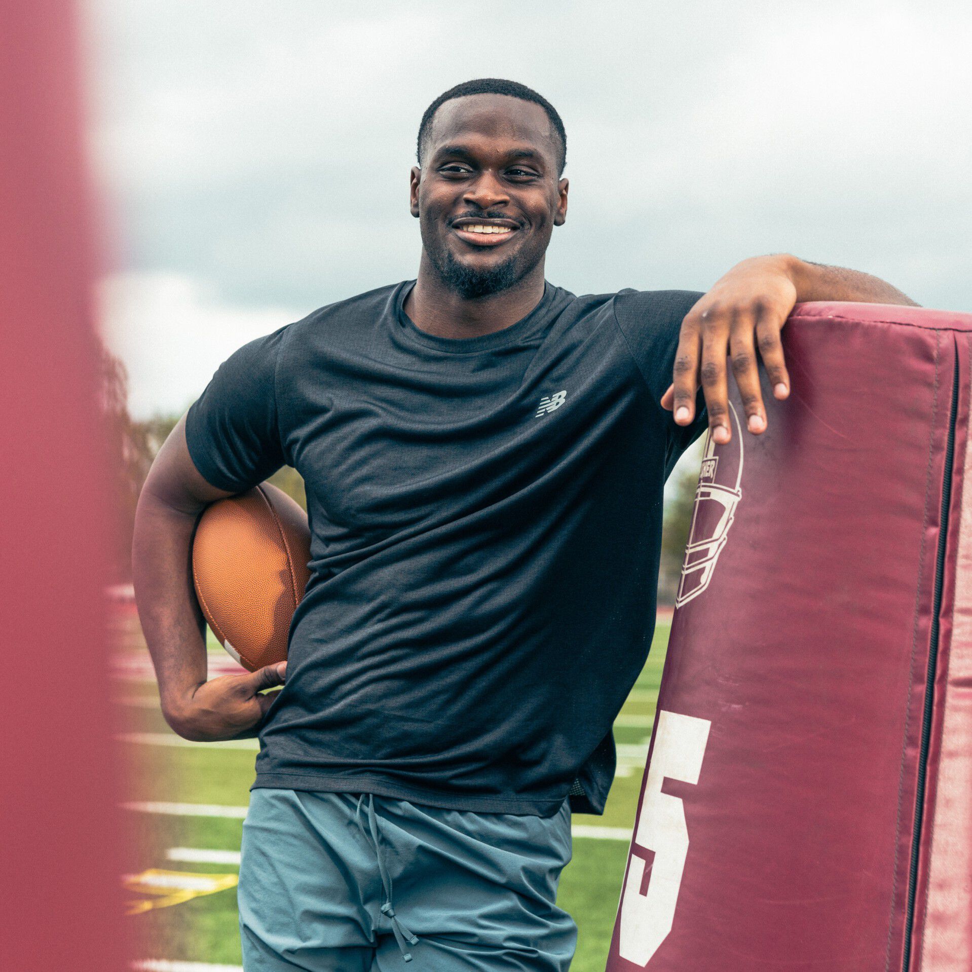 Young football athlete holding a football while leaning on a tackling dummy.