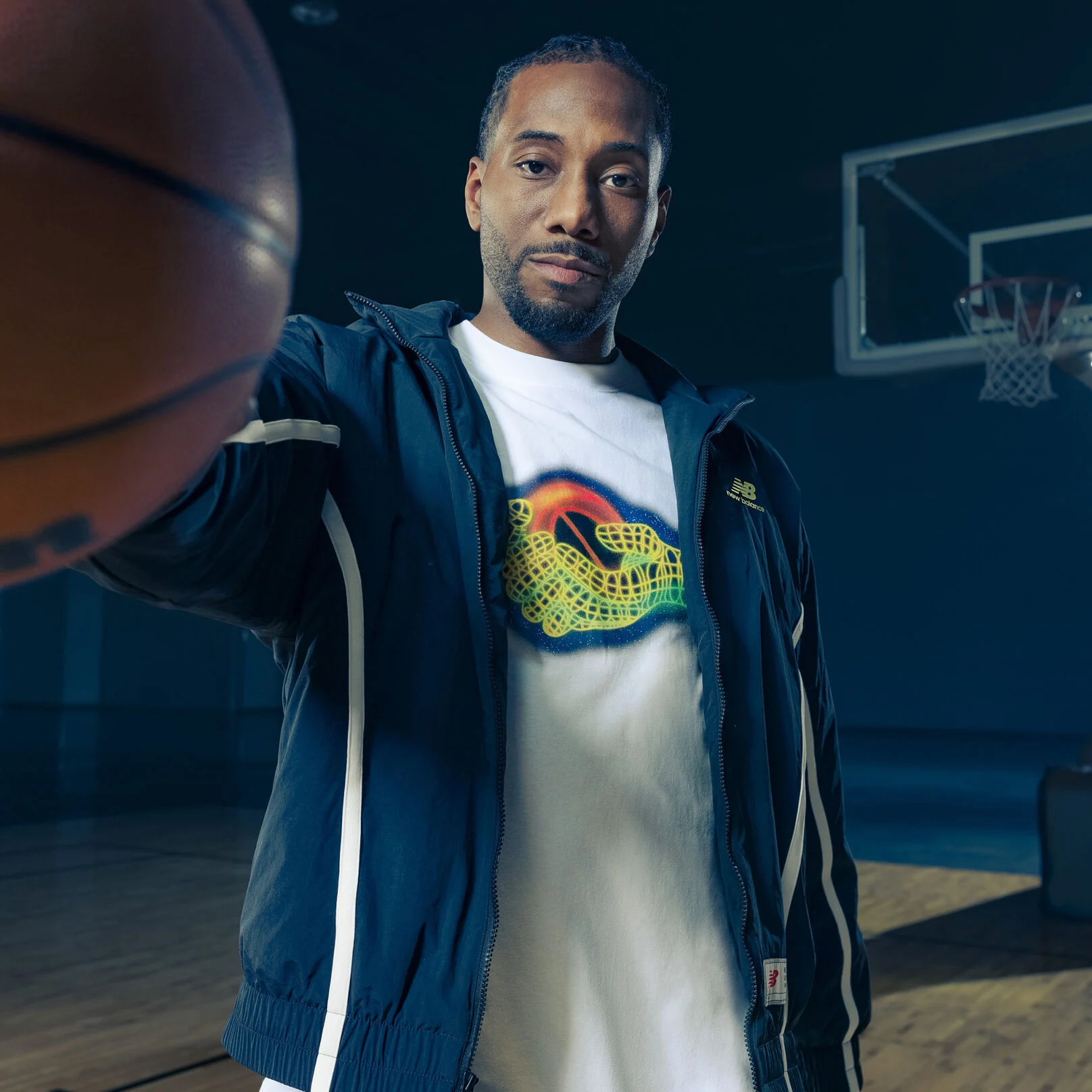 Kawhi wearing a navy jacket holding a ball to the camera.