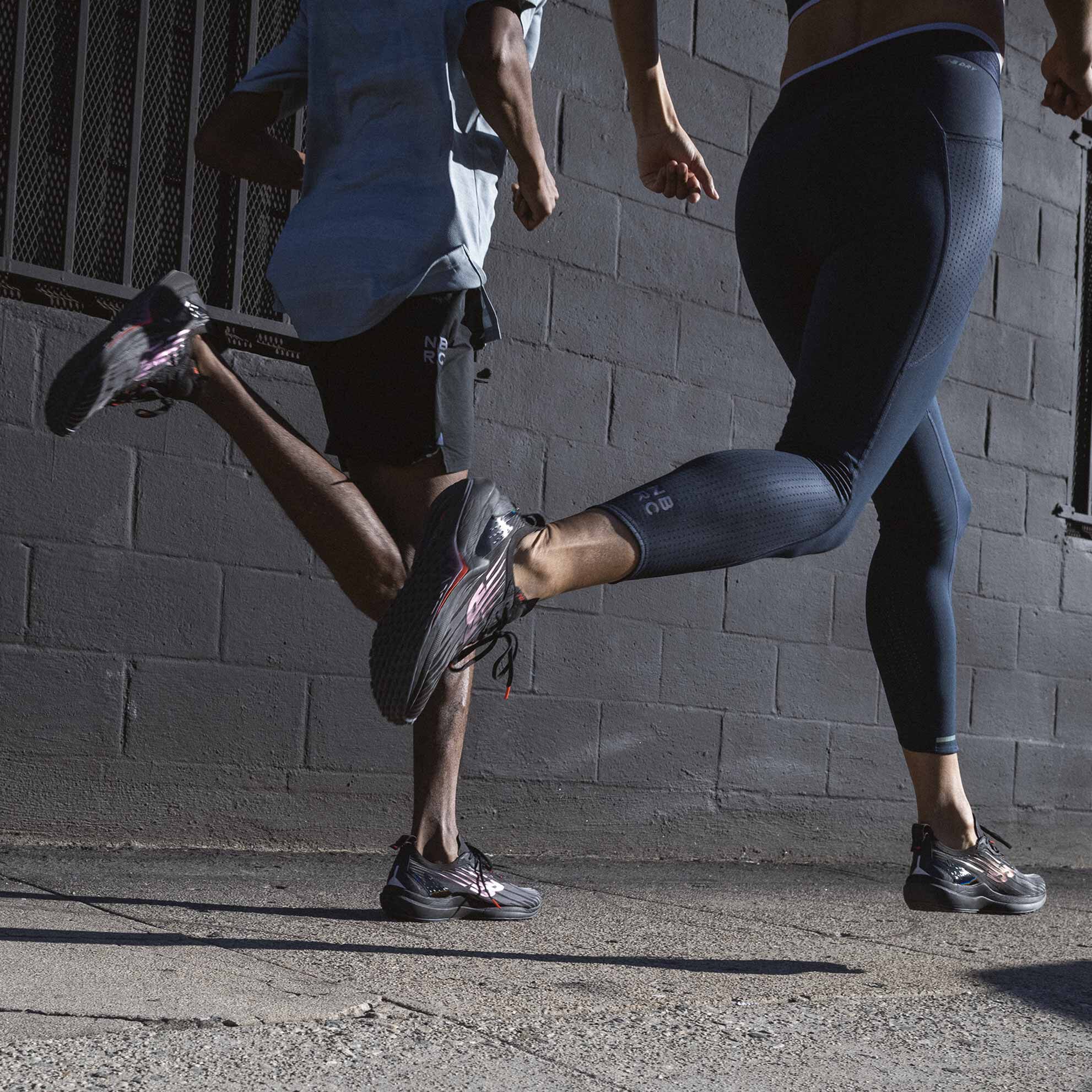 Un homme et une femme portant des chaussures de course FuelCell Speedrift courent sur le trottoir après la tombée de la nuit