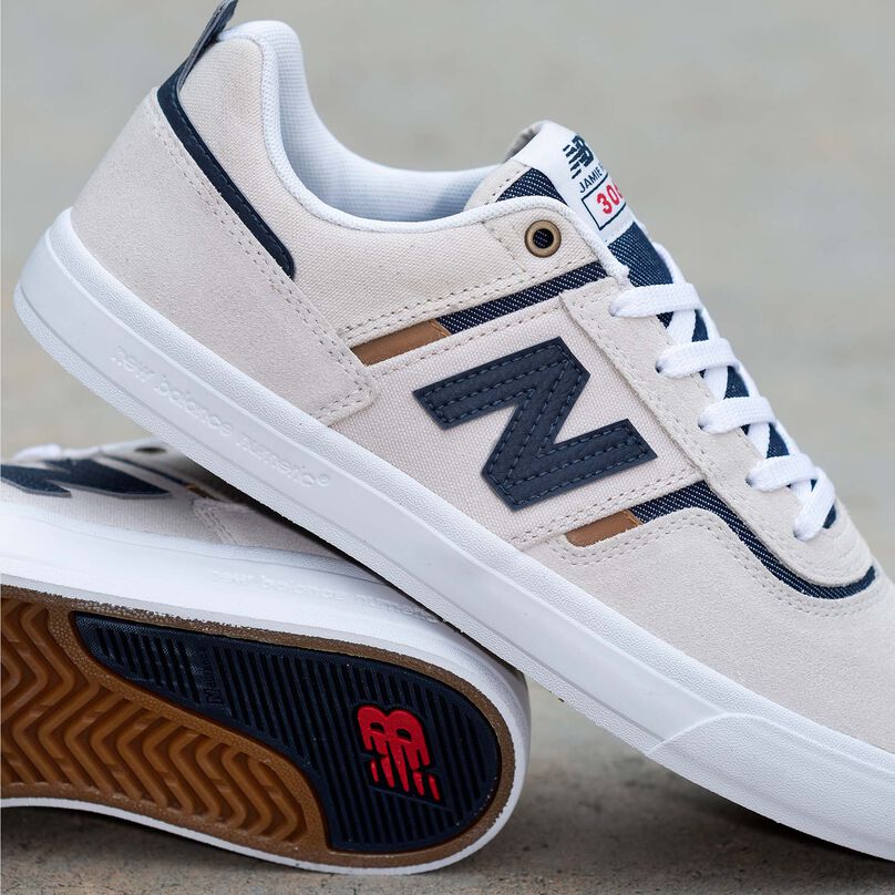 A cropped pair of laced cream-colored NB Numeric 306 skate shoes propped against one another sitting on concrete.