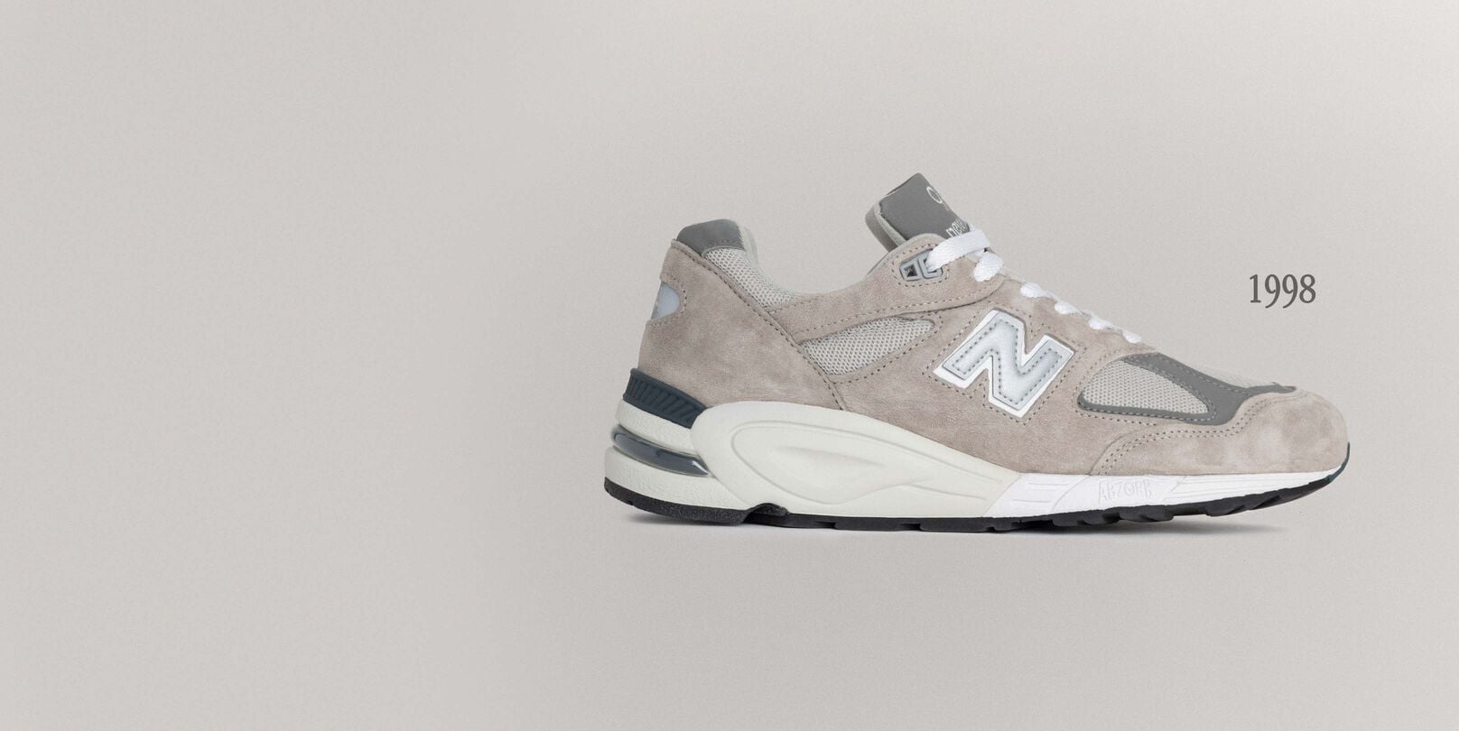 A grey 990v1 sneaker sitting on a grey background.