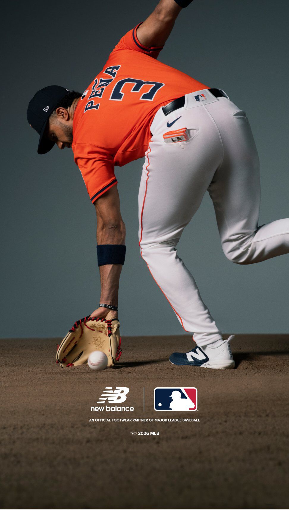 A baseball player wearing an orange jersey with the name &ldquo;PE&Ntilde;A&rdquo; and number 3 on the back is bending down to field a baseball on a dirt infield.