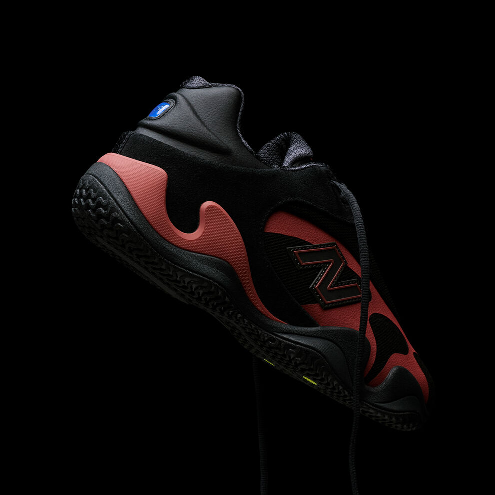 Close-up of a black and red athletic sneaker with visible branding, suspended against a black background.