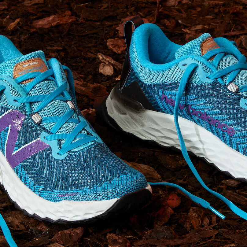 Close detail image of the pair of shoes with the laces untied sitting on dirt.