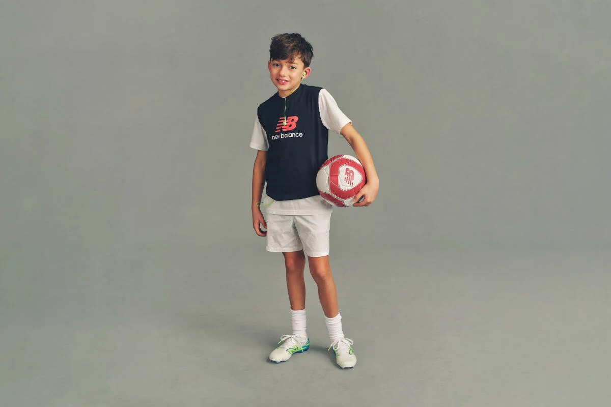 Close-up studio image of a child wearing a navy hooded sweatshirt with a &ldquo;New Balance Running&rdquo; logo printed on the chest.
