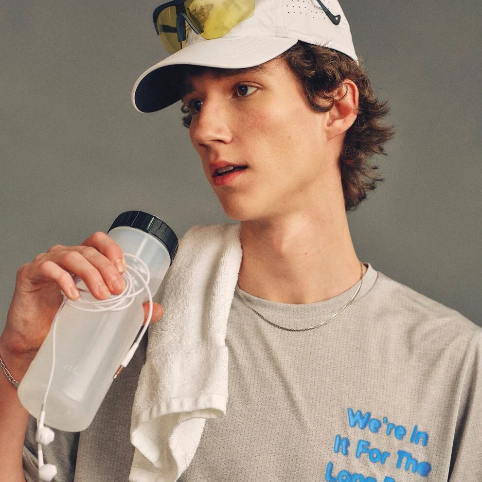 The person is wearing a light gray athletic T-shirt with blue text partially visible reading &ldquo;We&rsquo;re In It For The Long Run.&rdquo; 