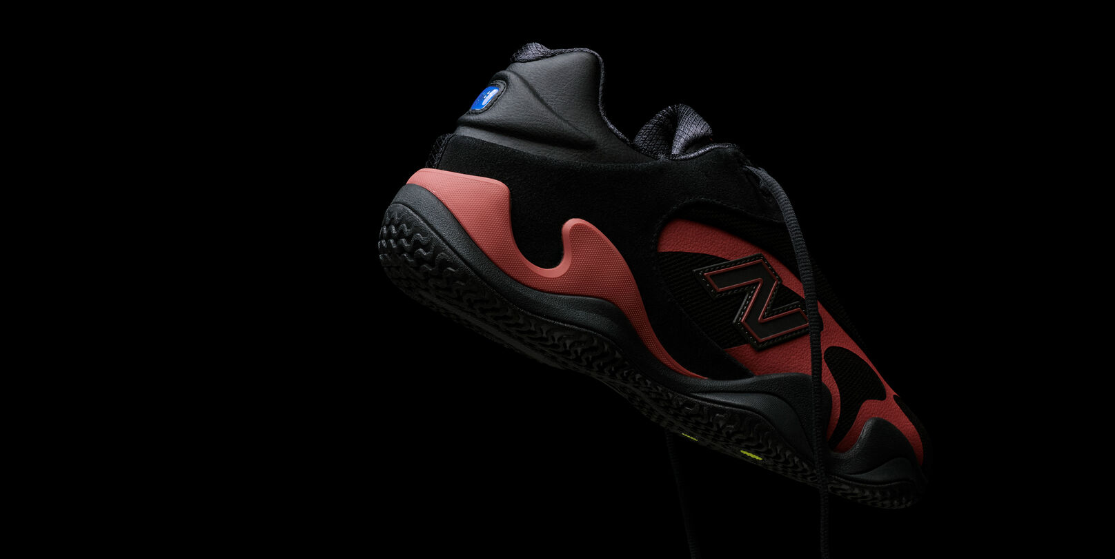 Close-up of a black and red athletic sneaker with visible branding, suspended against a black background.