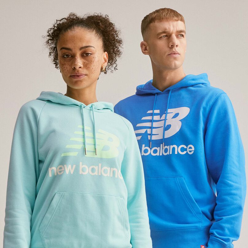 Un homme et une femme debout portant un sweat-shirt à capuche Essentials à logo Stacked.