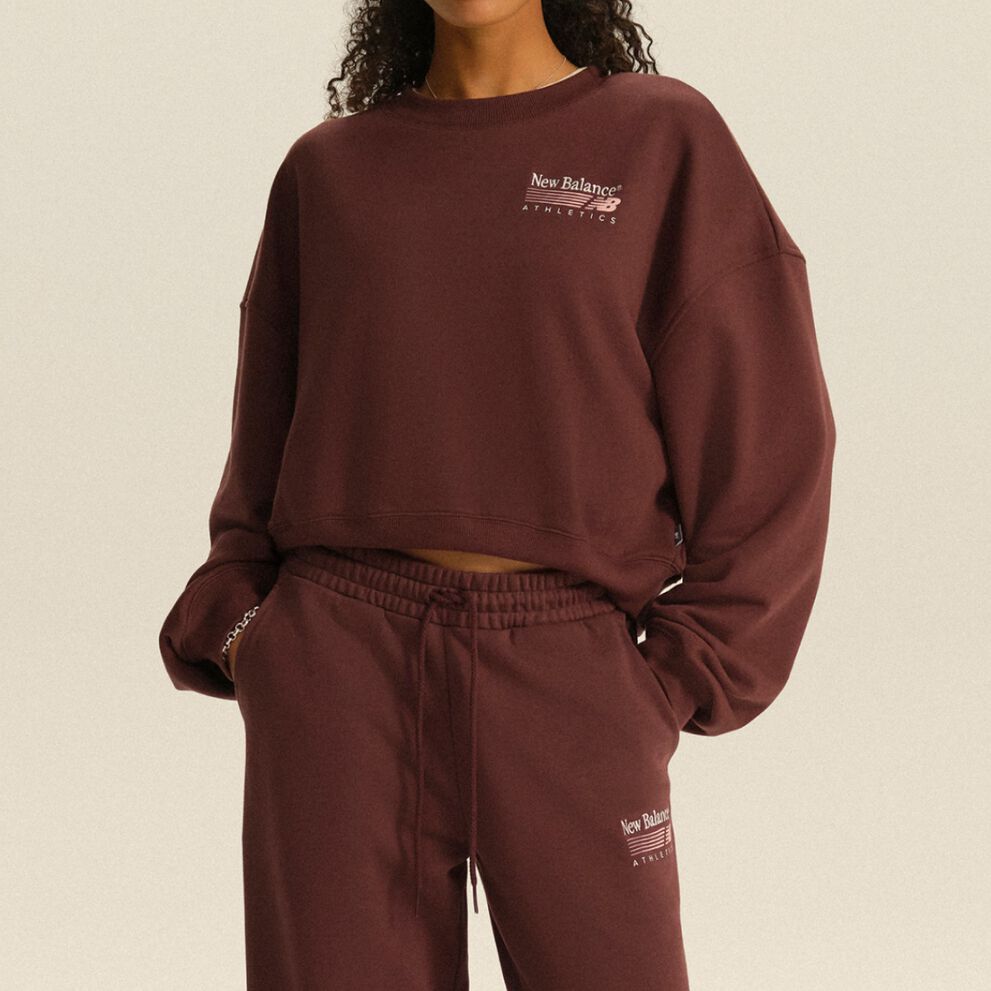 Personne portant un chandail molletonn&eacute; New Balance Athletics bordeaux et un pantalon de jogging assorti, dans un d&eacute;cor de studio &eacute;pur&eacute;.