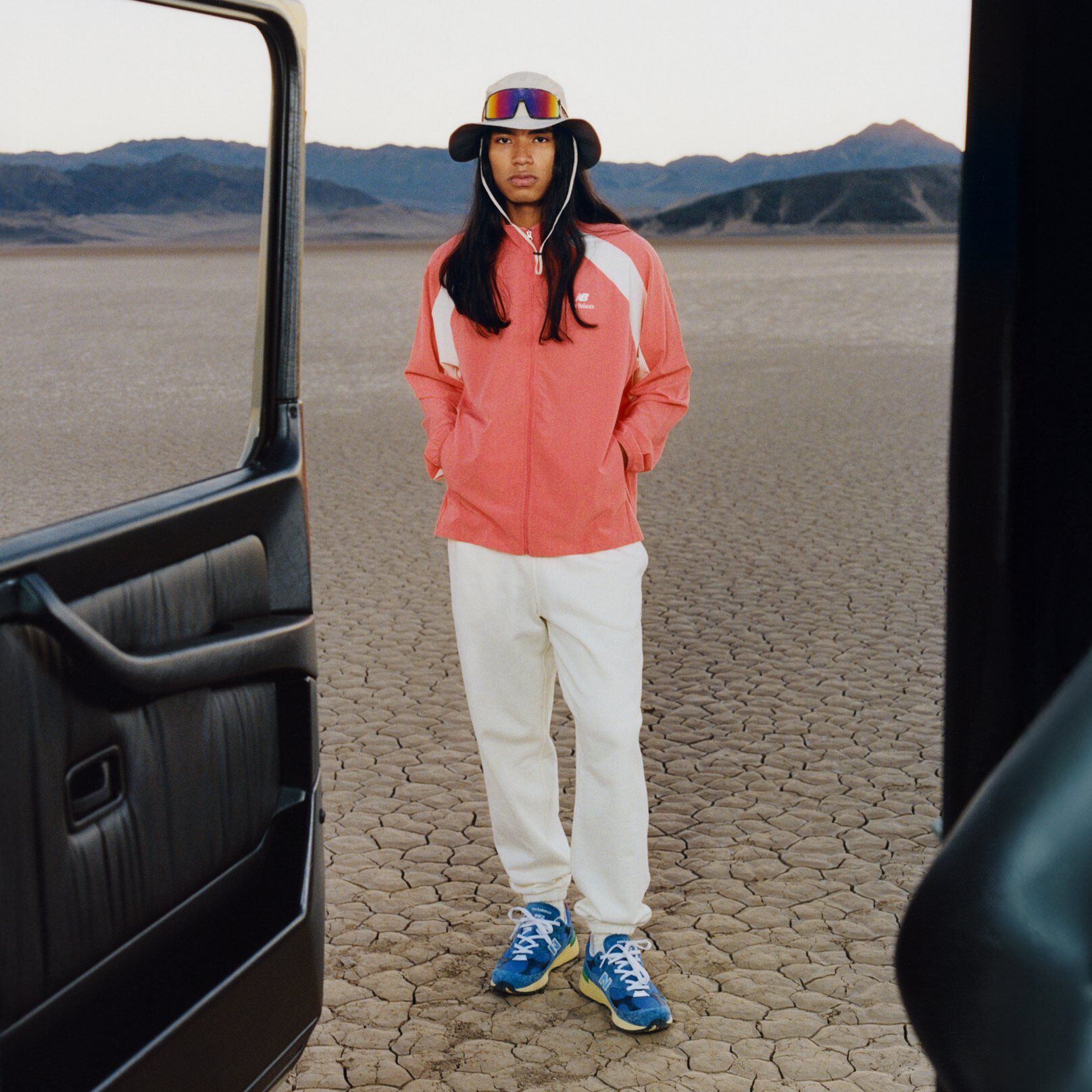 Un homme portant un chapeau seau et une veste orange, les mains dans les poches de sa veste.