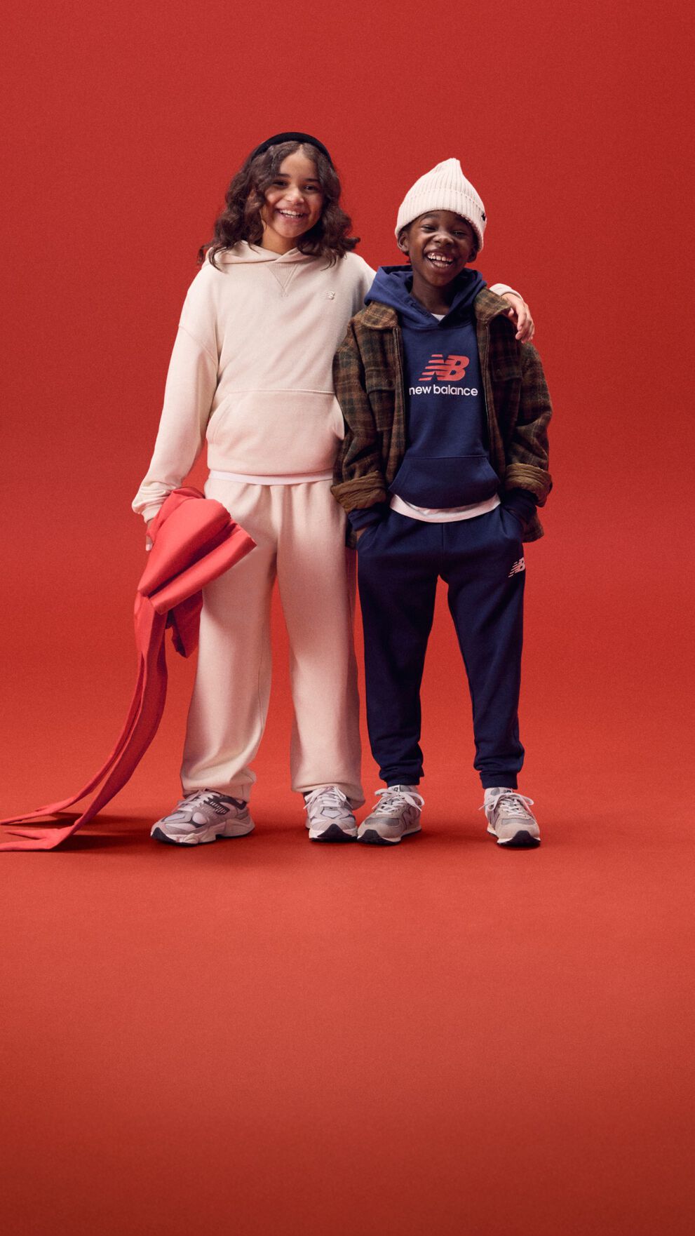 Deux jeunes enfants souriant, bras dessus sur un fond rouge.