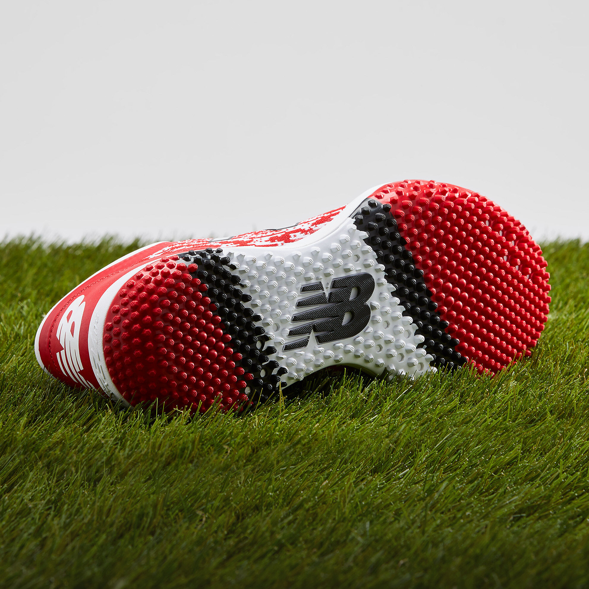 Bottom view of nubby outsole on the red 4040v5 Turf shoe sitting on grass
