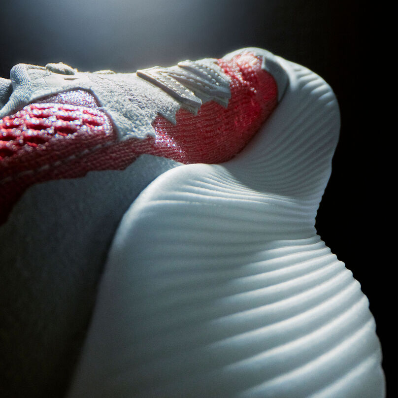 Une photo de détail dramatiquement éclairée du talon et de la tige intérieure d’une chaussure de course NB Stone Island Tokyo Design Studio gris clair FuelCell RC Elite avec des accents rouges