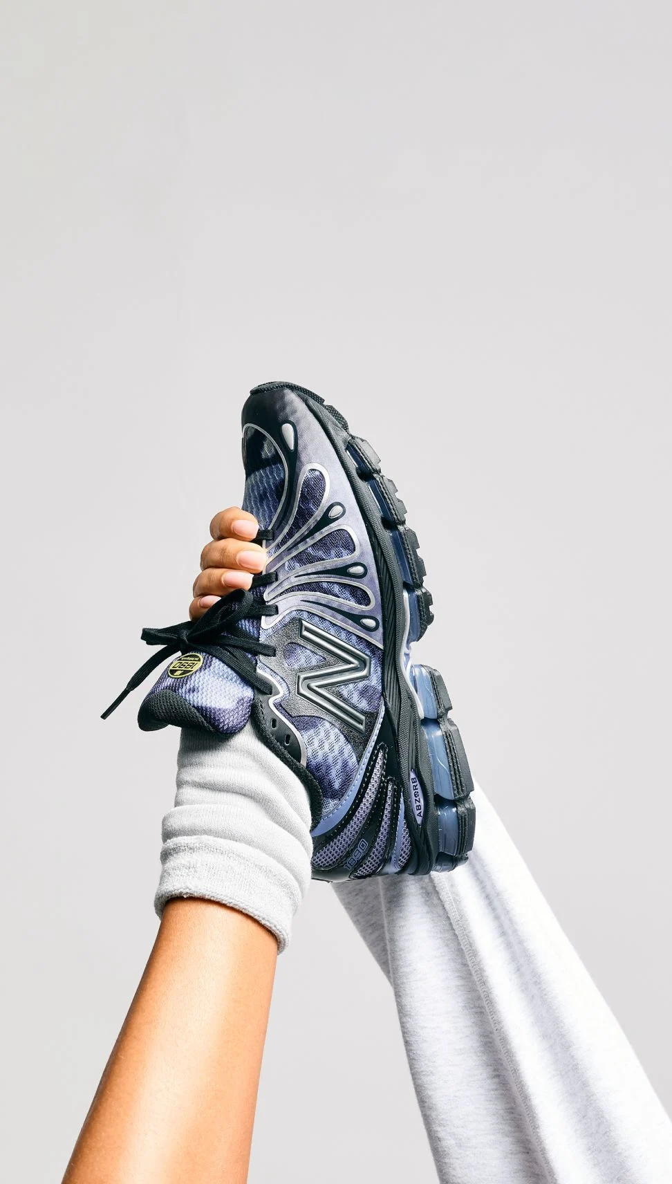 A person holding a blue pair of shoes in a hand while still wearing them.