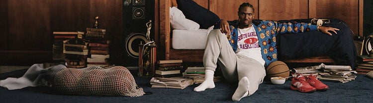 Tyrese Maxey sitting on a bedroom floor with a basketball and Hesi Lows