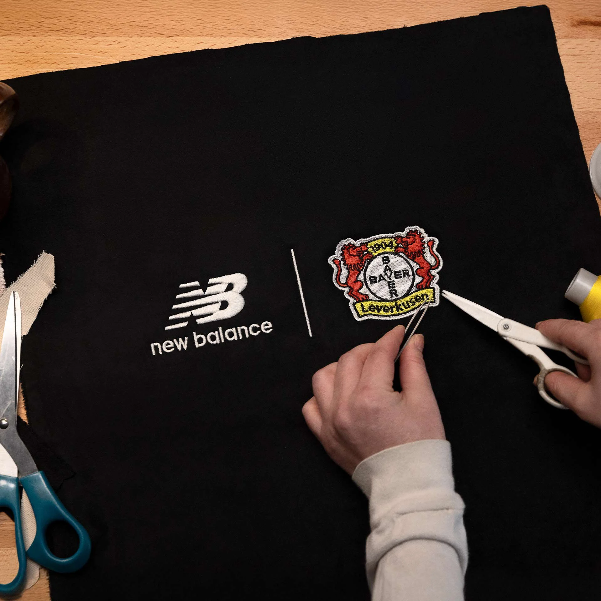 Embroidered lockup of the New Balance and Bayer 04 logos on fabric.