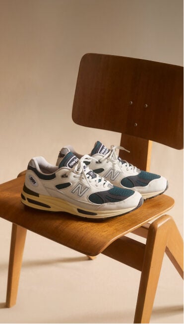 Une paire de baskets New Balance Made in UK pos&eacute;e sur une chaise en bois dans un environnement de studio beige.