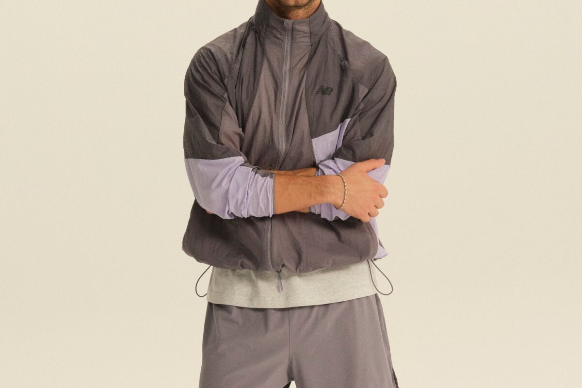 Person wearing a gray and lavender color-block performance jacket and gray athletic pants in a clean studio setting.