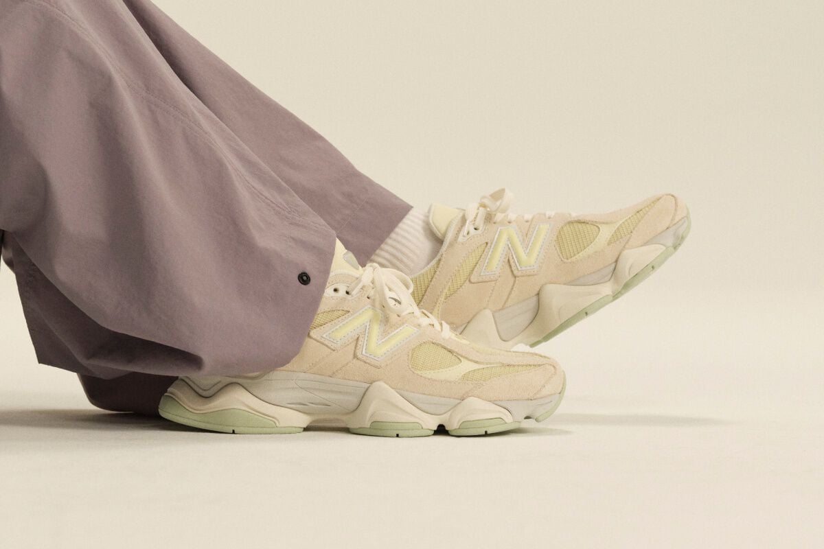 Gros plan sur des chaussures de sport New Balance cr&egrave;me port&eacute;es avec des chaussettes blanches mi-mollet et un pantalon lavande &agrave; jambes larges, dans un d&eacute;cor de studio &eacute;pur&eacute;.