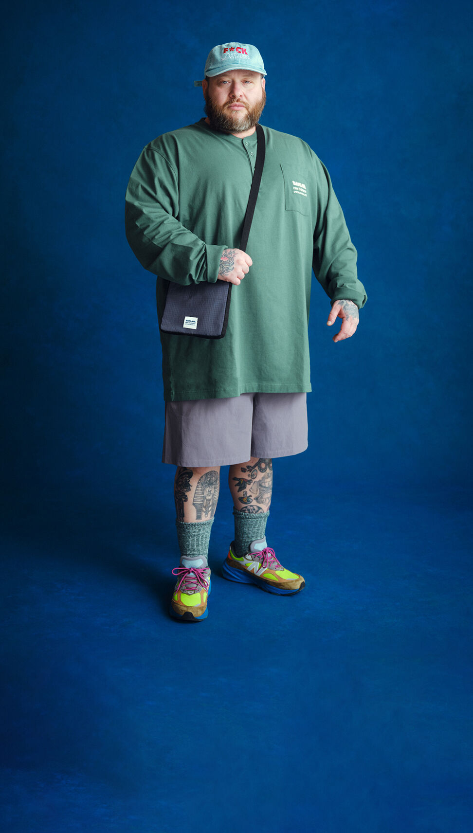 Young man standing up wearing a green long sleeve tshirt on a blue background.    
