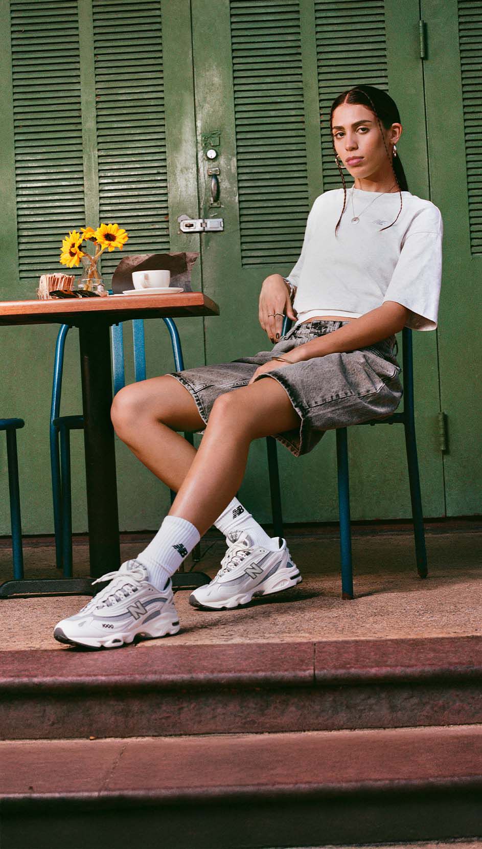 Un individu, assis à la table d'un café, portant une paire de chaussures New Balance 1000. 
