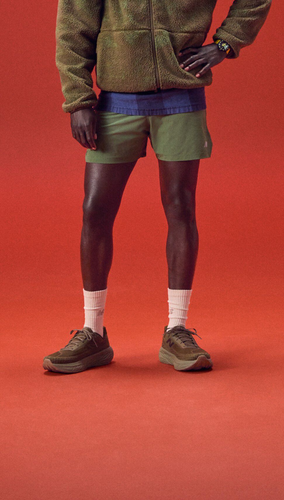 Jeune homme debout sur un fond rouge, portant un hoodie vert.