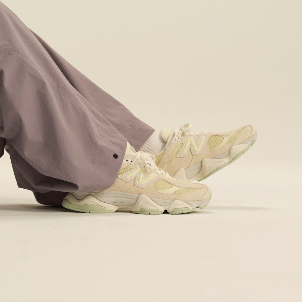 Gros plan sur des chaussures de sport New Balance cr&egrave;me port&eacute;es avec des chaussettes blanches mi-mollet et un pantalon lavande &agrave; jambes larges, dans un d&eacute;cor de studio &eacute;pur&eacute;.