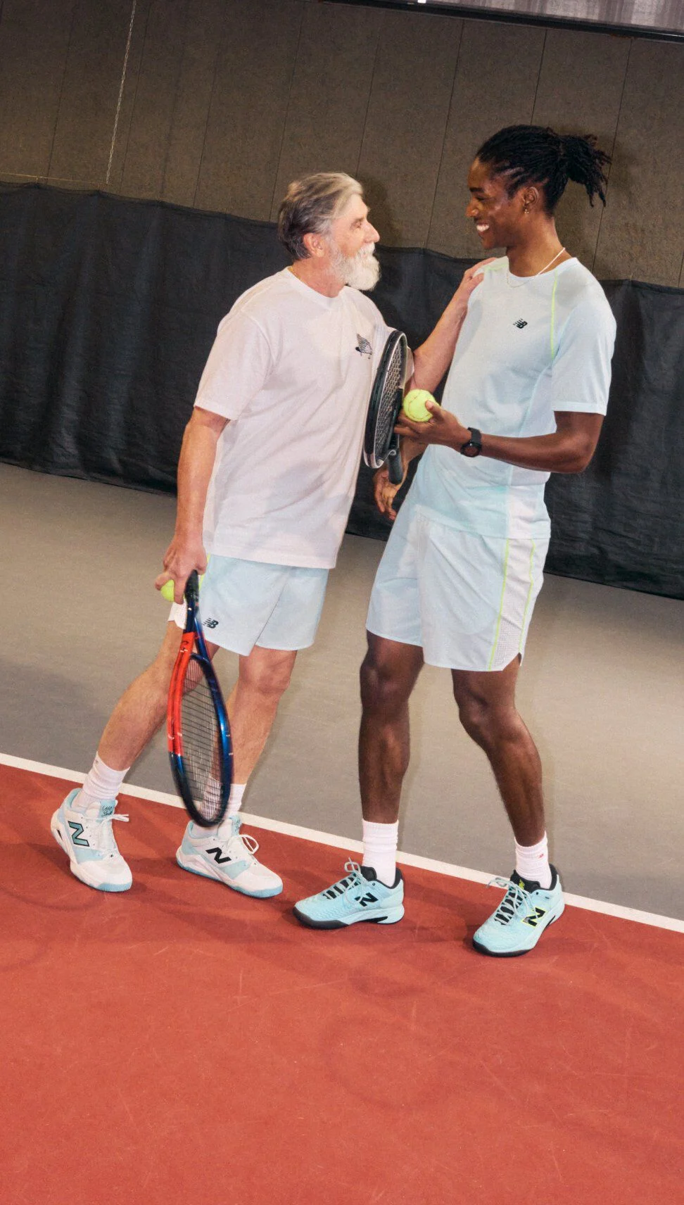 A tennis player stands on an indoor court wearing a black athletic outfit and white sneakers.