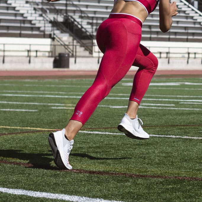 Back view of Sydney McLaughlin’s legs running on field wearing white FuelCell Prism running shoes
