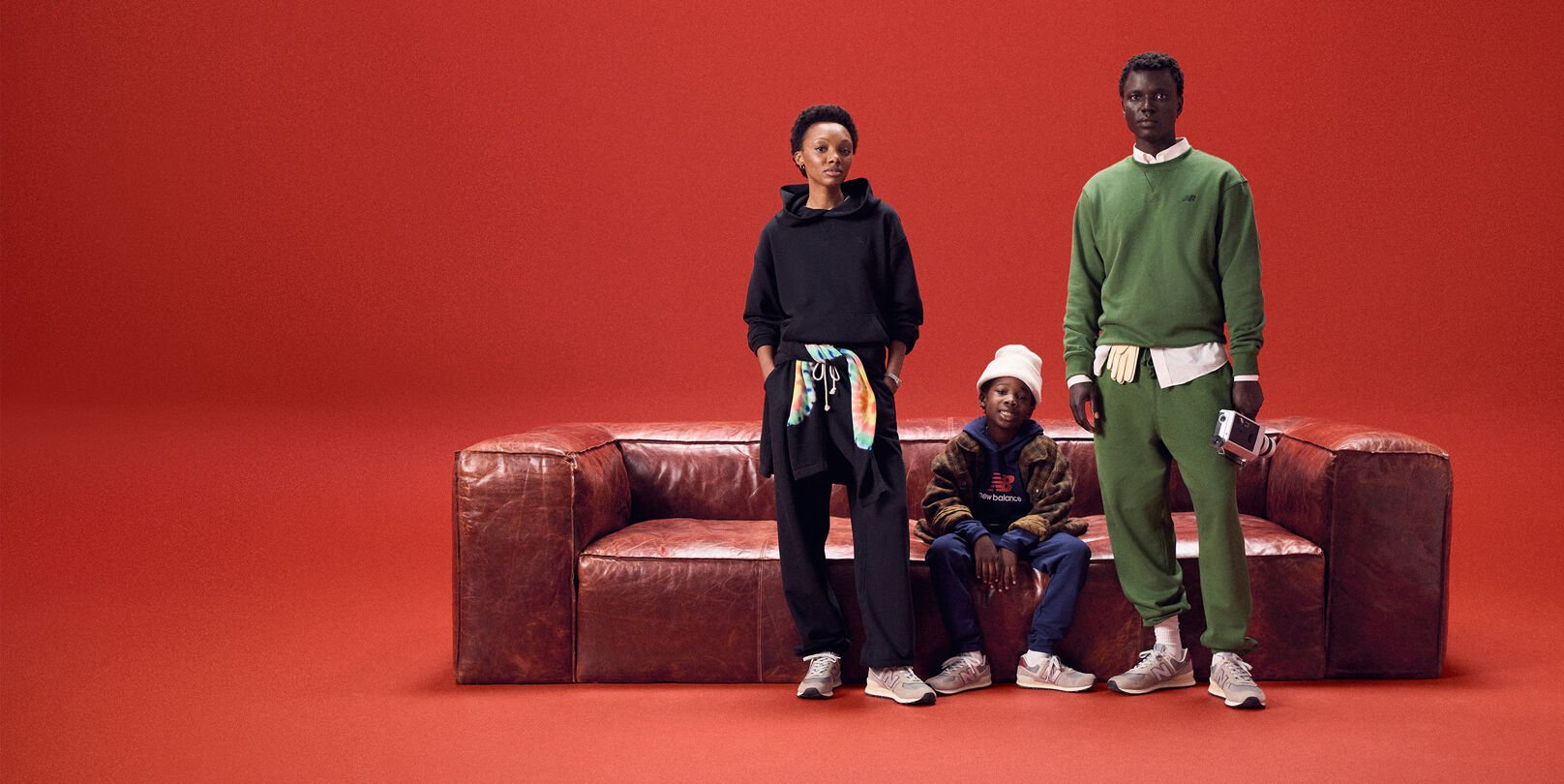 Family of three sitting on a red leather couch on a red background.