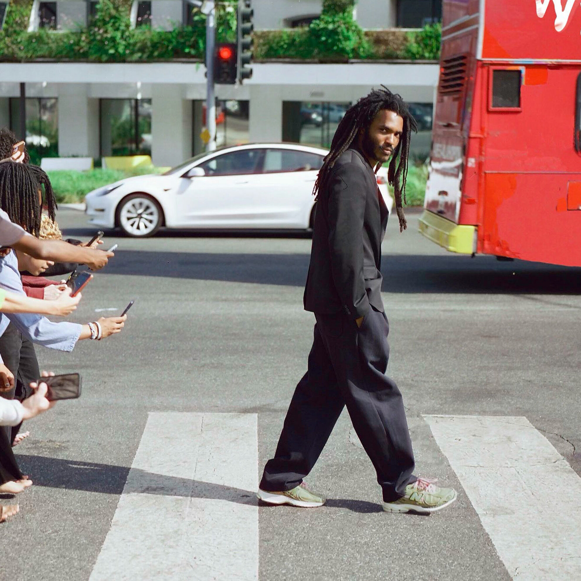 Man walking in a black suit on a road followed by a crowd of paparazzi