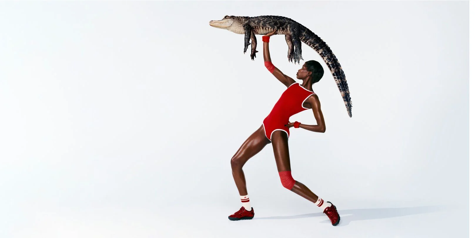 Une femme devant un fond blanc, portant les chaussures Gator Run et tenant un alligator.