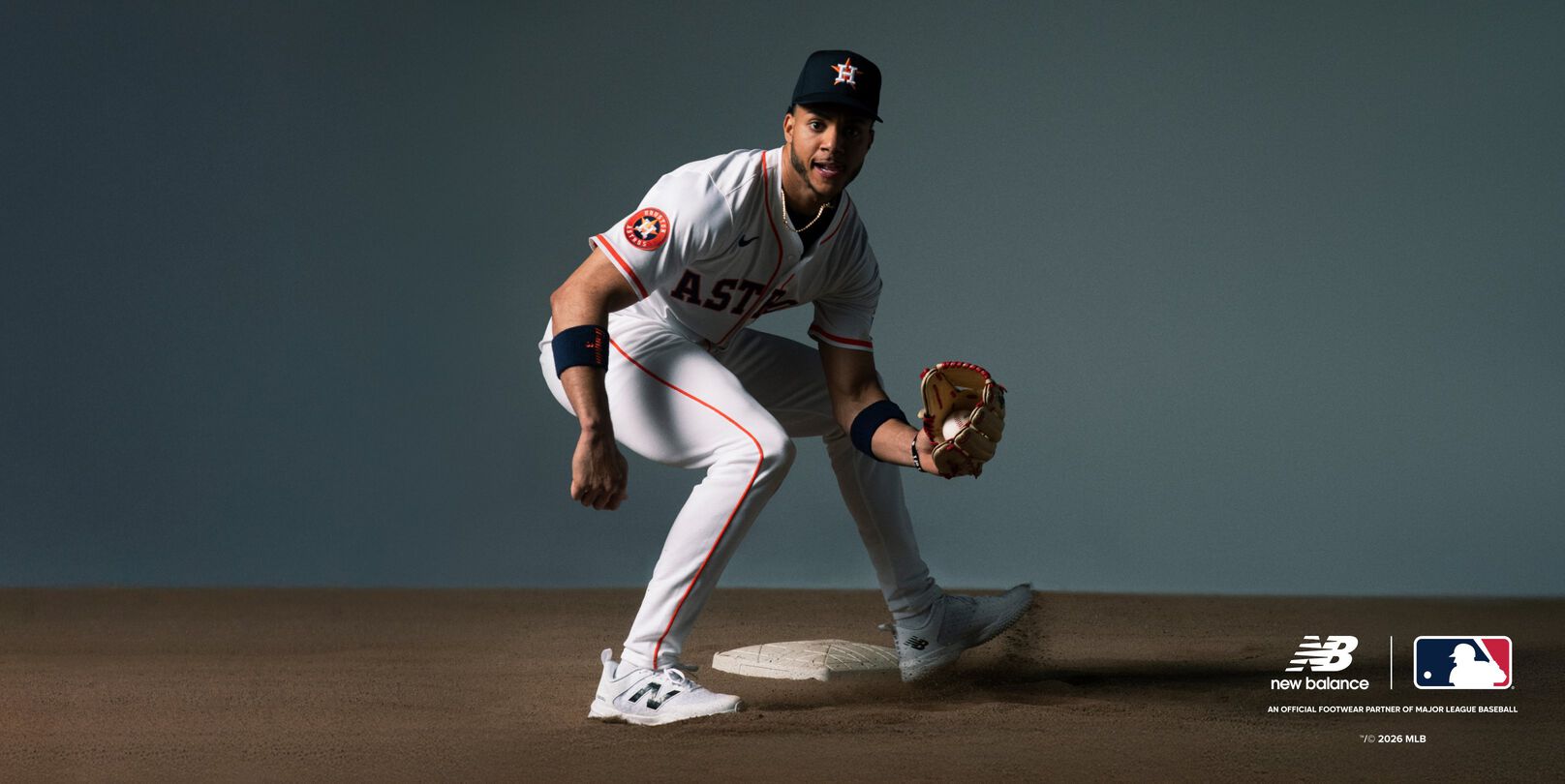 A baseball player wearing a white Houston Astros uniform with orange accents is in a ready fielding stance on a dirt infield.