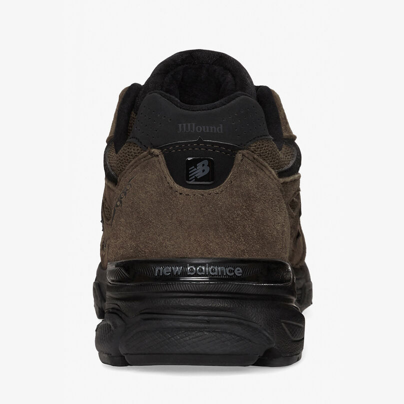 Paire de chaussures 990v3 marron posées sur un fond de studio gris, vue de dos pour souligner les détails du talon
